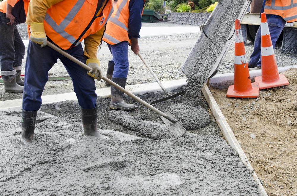 Group of builders working together on pouring cement during an upgrade of public projects to fix residential street pavement.